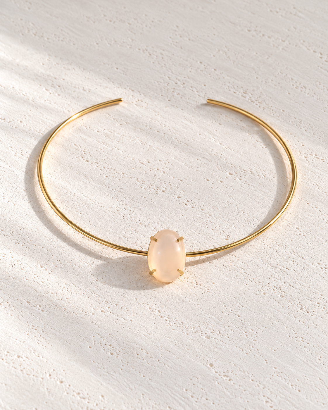 Collar Louise rígido dorado con piedra sobre cemento blanco